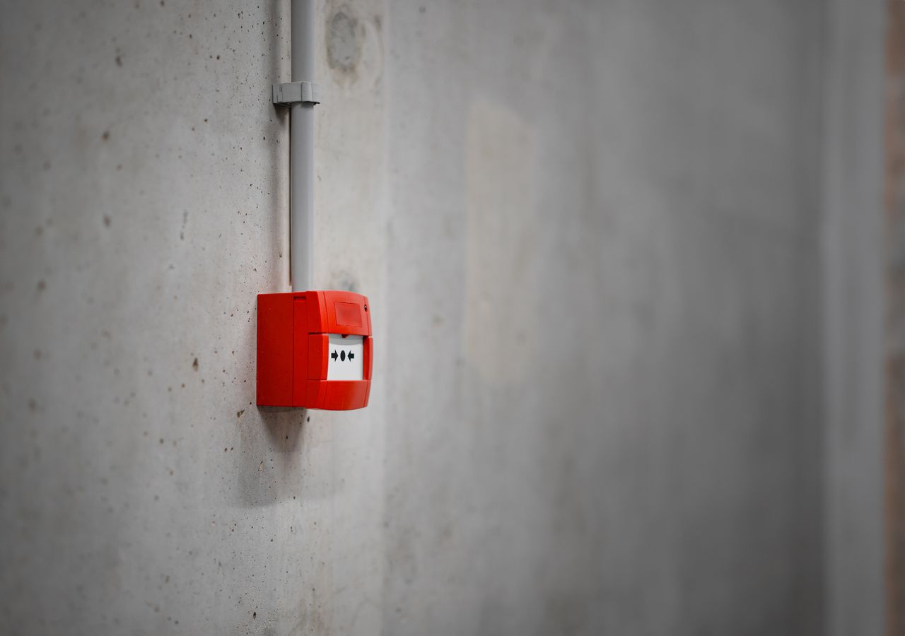 Mastering the First Impression: Your intriguing post title goes here A red alarm box mounted on a gray concrete wall, offering urban security.